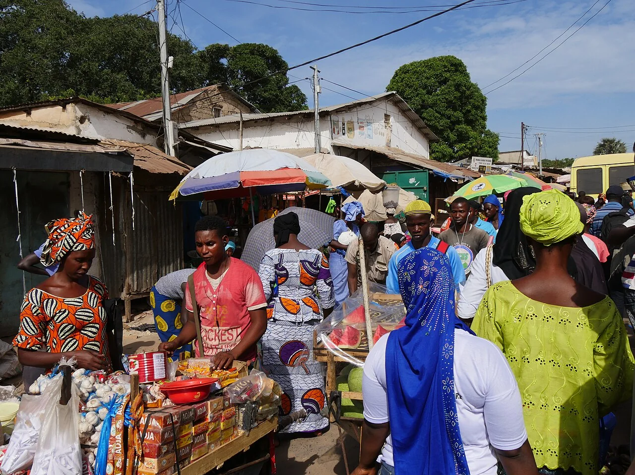 Colourful stalls and shoppers along a market lane in Serekunda